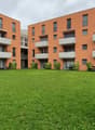 Two buildings with five floors, balconies, greenery in front, one table, two chairs, green lawn.