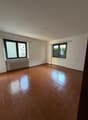 Empty room with tile flooring, white walls, two large windows with black frames, white radiators, and an electrical outlet.