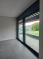 Spacious room with large windows offering a scenic view, grey tiled flooring, and dark-colored walls.