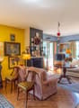 Living room with fireplace, yellow and blue walls, a TV, multiple paintings and frames, a carpet, a desk, a couch, and chairs