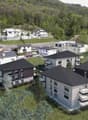 Group of modern townhouses, black rooftops, multiple balconies, surrounded by greenery, hilly background