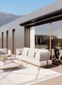 Outdoor seating area with a white rug, a wooden coffee table, and cushioned chairs and a sofa. There is also a dining table and chairs for indoor dining, both covered with white curtains. There are windows allowing for views of the outside.