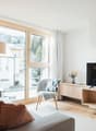 modern design, floor-to-ceiling windows, wooden floor, comfortable seating, neutral color palette, decorative vase, TV