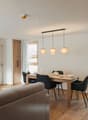 Wooden table and chairs, dining set, lamps hanging from the ceiling, couch, wooden floor, white walls, door, and window