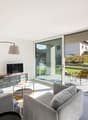 modern living room with sliding glass doors, large windows, gray couches, glass table, yellow pillows, TV, floor lamp, balcony with chairs and table