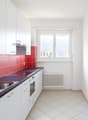 Modern kitchen with white cabinets, red tile backsplash, stainless steel sink, and dishwasher. The kitchen has a window and tiled flooring.