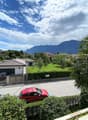balcony with view, several cars parked, small house with garage, mountainous landscape, trees