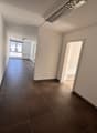 Empty hallway with brown tiled flooring, white walls, windows, and ceiling lighting