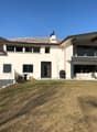 Modern two-story white house on a hill, flat roof, double-story balcony with railings, large lawn in front, trees and mountains in the background.
