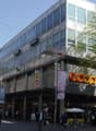 Modern building with glass facade, large sign reading 'COOP', multiple floors, people walking in front