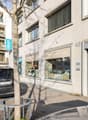 Two-story residential building, modern design, shops on the ground floor, balcony on the upper floor, white facade, parking space