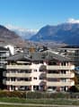 Aerial view of a residential building complex with multiple buildings, surrounded by greenery and mountains in the background.
