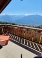 wooden balcony with lounge chair, wooden railing, panoramic mountain view, grassy slope below
