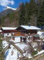 chalet style house, wooden exterior, snow covered roof, balcony, surrounded by trees and mountains
