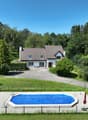 House with brown roof, white walls, swimming pool, driveway, fenced area, green landscape