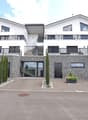 2 story modern house, white and grey exterior, two garages, balconies on each floor, planted area in front