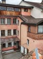 Multiple buildings with balconies, brick and wood construction, various window sizes, red shutters