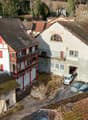 Aerial view of a house with a garage, multiple windows, red shutters, and surrounded by other houses and cars