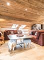 room features wooden ceiling and hardwood floors, couch with pillows, table, chairs, kitchen and dining area visible in the background