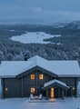 Wooden log cabin in a snowy mountainous landscape with a view of a lake