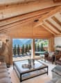 Living room with wooden walls, large windows, fireplace, glass table, couches, armchairs, and decorative items