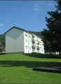 3-story apartment building with green exterior, surrounded by a grassy lawn and trees
