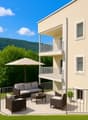 Apartment building with beige walls, multiple balconies, patio with outdoor furniture, a sofa, a table, an umbrella and a plant in a pot.