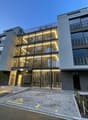 Contemporary apartment building with 4 floors, balconies, grey walls, and illuminated signage, private parking.