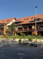 Apartment building with brown roof, balconies, large windows, stone wall, and trees in front
