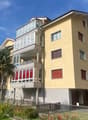 5-story apartment building, yellow exterior, multiple balconies, gated entrance, red-framed windows, red roof