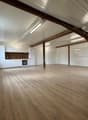 Empty room with wooden beams, wooden floors, white walls, modern kitchen, radiators, and an open window.