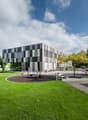 Modern architectural building with checkered facade, located outdoors, surrounded by a lawn, playground, and trees.