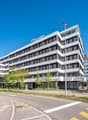 Office building, white exterior, glass windows, multiple floors, sign reading 'office-center', trees, streetlight, cars parked on side, street with pedestrian lane and crosswalk, traffic signal