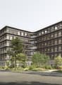 5 story building, multiple windows, balconies on some windows, green plants and trees around, empty street