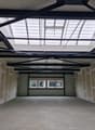 Empty room with concrete floor, unfinished walls, metal roof structure, and windows