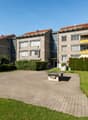 Multi-story apartment building with brick and concrete construction, balconies, and a landscaped courtyard with a paved walkway and benches.