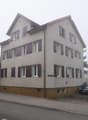 Gray apartment building with multiple windows, brown base, streetlight and parking in front