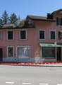 2-story pink and white buildings with slanted roofs, windows, and a storefront on the ground floor. There is a parking area in front of the buildings with a red and white barrier.