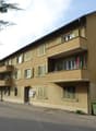 3-story apartment building, beige wall, green windows, multiple balconies, garage at the entrance