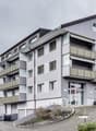 Multi-storey building with multiple balconies and windows, car parking area in front