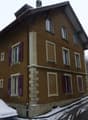 2 story house, brown exterior, white windows, purple shutters, chimney, front yard with snow, 3 cars parked in front
