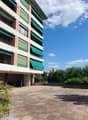 Large building with multiple floors, brick facade, multiple balconies, parking area, green awnings