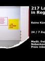The image shows a storage room or warehouse space. The room has white walls, a red door, and signage on the wall indicating that there are 217 storage spaces available in Regensdorf. The signage also mentions that there is 24/7 access and that all additio
