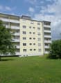 4 story building, yellow exterior, balcony on each floor, green lawn, trees