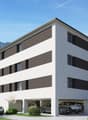 3-story modern apartment building with a flat roof, white and gray exterior, large windows, and a ground-level parking garage with spaces for multiple vehicles.