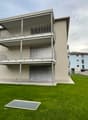 3-story modern apartment building with balconies, garage, and grassy lawn area in front
