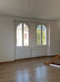 Spacious living room with large arched windows, hardwood floors, and a modern kitchen area with black cabinets.