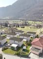 Cluster of modern houses, each with a garage, set in a green landscape with a mountain in the background