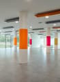 spacious room, white pillars, orange, green, and pink stripes on pillars, tiled floor, large windows, reflective surface
