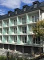 3-story apartment building with white exterior, glass balconies, and black roof dormers
